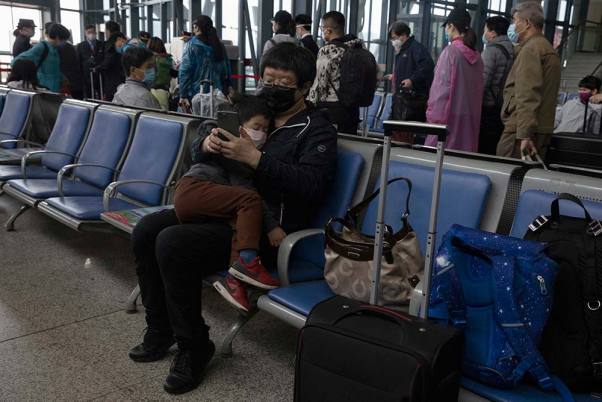 गोद में अपने बच्चे को लेकर मध्य चीन के हुबेई प्रांत में वुहान से बीजिंग के लिए रवाना होने वाली ट्रेन का इंतजार करता एक यात्री