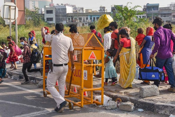 लॉकडाउन के बीच अपने मूल स्थानों तक पैदल के जाने के दौरान प्रवासी श्रमिकों को दिल्ली-यूपी बॉर्डर पार करने से रोकता पुलिसकर्मी