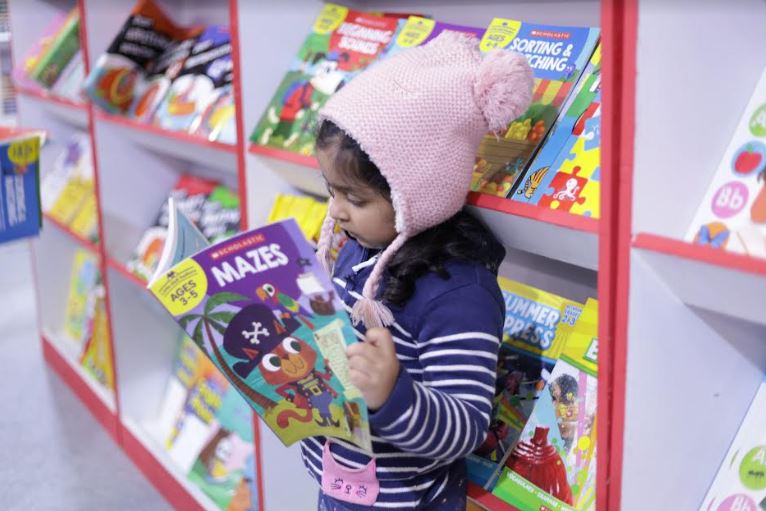 दिल्ली के प्रगति मैदान में पुस्तक मेले में किताब पढ़ने में मगन नन्ही सी बच्ची