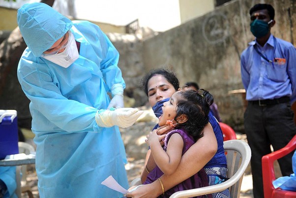 मुंबई में धारावी के कल्याणवाड़ी में कोविड-19 टेस्ट के लिए एक बच्चे के मुंह से स्वैब सैंपलिग लेता डॉक्टर