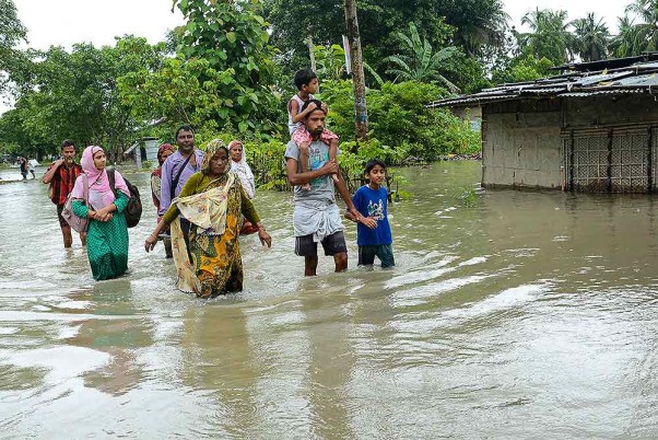 असम के कामरूप जिले में बाढ़ वाले क्षेत्र से सुरक्षित स्थान पर जाते ग्रामीण