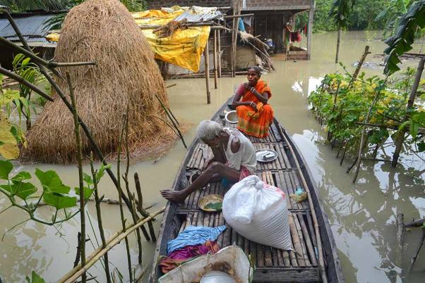 बाढ़ प्रभावित कामरूप जिले के चंद्रपुर में अपने आंशिक रूप से जलमग्न घर के सामने एक नाव पर बैठे ग्रामीण