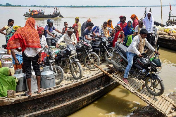 पटना में गंगा नदी पार करने के बाद नाव से अपने वाहनों को उतारते लोग