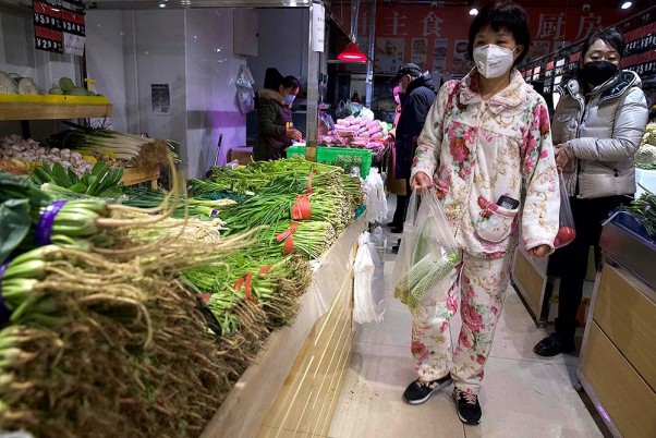 चीन के बीजिंग में सब्जियों की दुकान के सामने खड़ी मास्क पहनी महिला