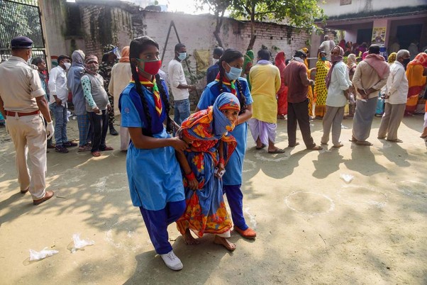 बिहार विधानसभा चुनाव के तीसरे चरण के मतदान के दौरान वैशाली जिले के महुआ में एक मतदान केंद्र पर अपना वोट डालने के लिए एक बुजुर्ग मतदाता को ले जाती स्कूली छात्राएं