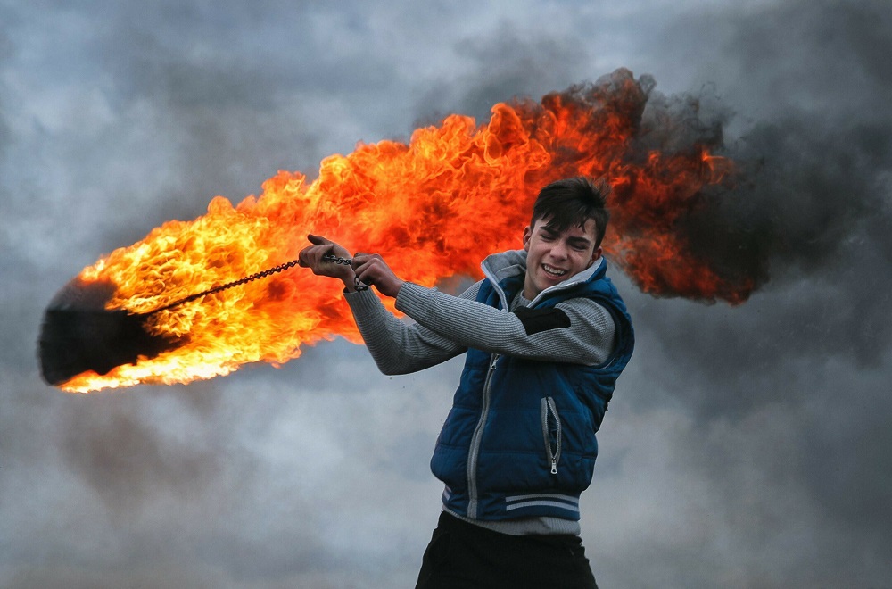 रोमानिया के पोपलाका में एक अनुष्ठान के दौरान धातु की चेन पर जलता हुआ टायर बांधकर घुमाता युवक