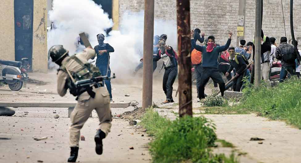श्रीनगर में एक कॉलेज के बाहर पत्थरबाजी करते प्रदर्शनकार‌ियों पर आंसू गैस बरसाने के बाद जवाबी पत्थर फेंकता पुल‌िसवाला